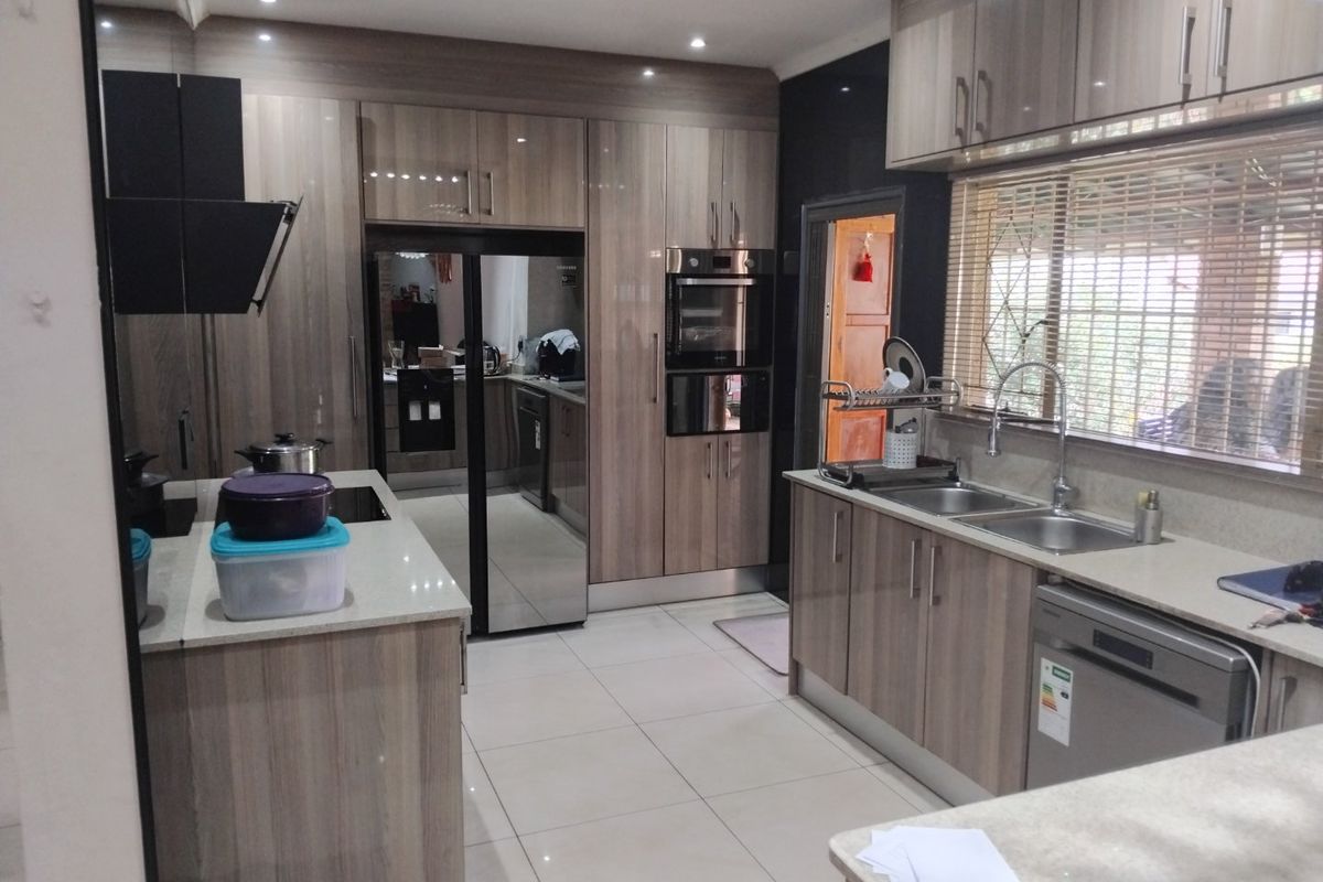 Modern kitchen featuring wood-grain cabinetry, stone countertops, integrated oven, extractor fan, and a double sink with a view through the window.