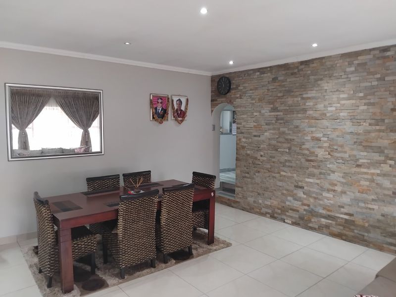 A well-maintained dining room featuring a prominent stone-clad feature wall, recessed downlighting, and neutral tiled flooring.