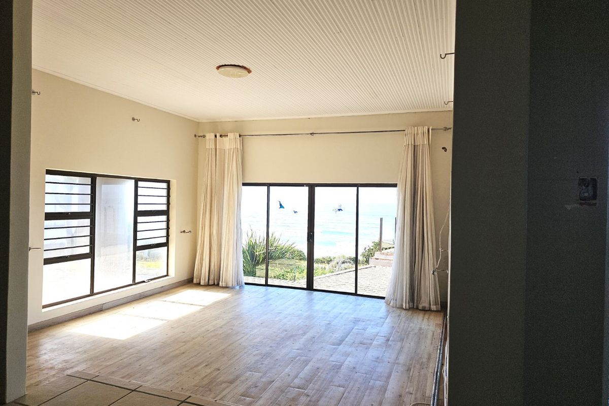 Spacious living area featuring wood-look flooring, large windows, and sliding glass doors that provide natural light and views of the ocean.