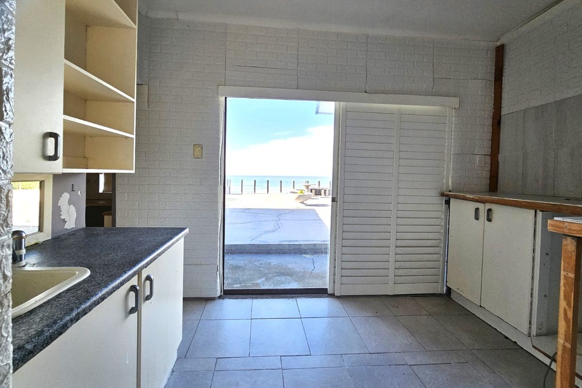 A dated kitchen area featuring built-in cabinetry and tiled flooring, with direct access to an outdoor patio area overlooking the ocean.