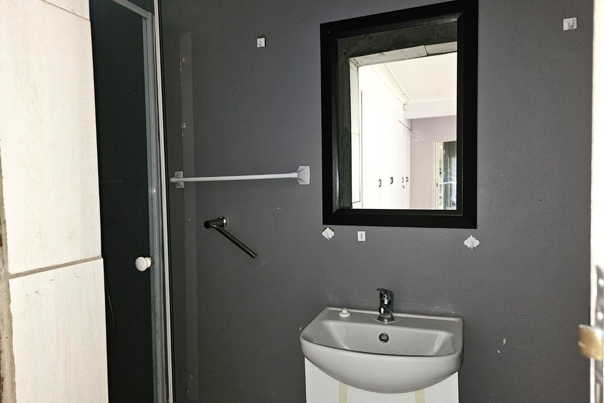 A bathroom featuring a wall-mounted vanity basin, a framed mirror, and a shower enclosure with dark grey wall finishes.