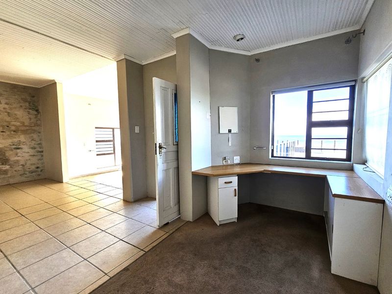 A functional home office space featuring built-in cabinetry, tiled and carpeted flooring, and natural light, with an adjacent room visible.