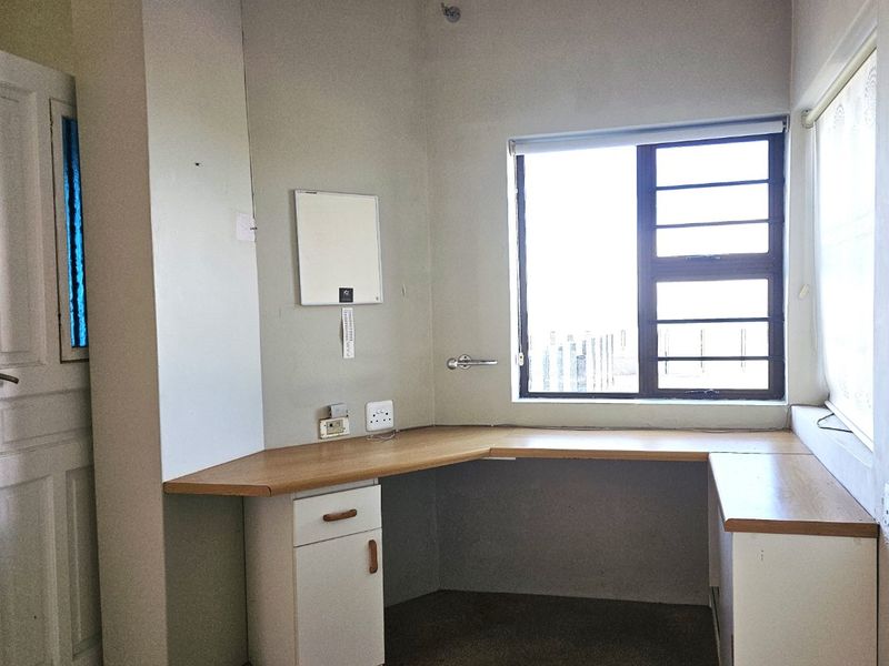 A functional home office space featuring built-in corner desk cabinetry, ample natural light from large windows, and neutral wall finishes.