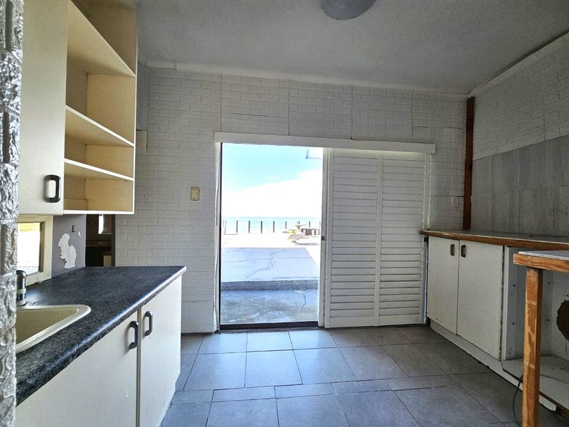 A dated kitchen area featuring built-in cabinetry and tiled flooring, with a sliding door providing direct access to an outdoor patio and sea view.