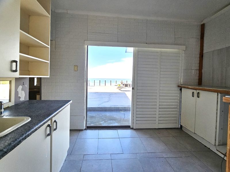 A dated kitchen area featuring built-in cabinetry and tiled flooring, with direct access to an outdoor patio area overlooking the ocean.