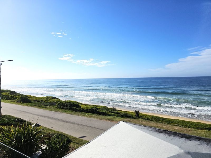 A scenic elevated view overlooking the coastline, featuring the ocean, sandy beach, and adjacent coastal road.