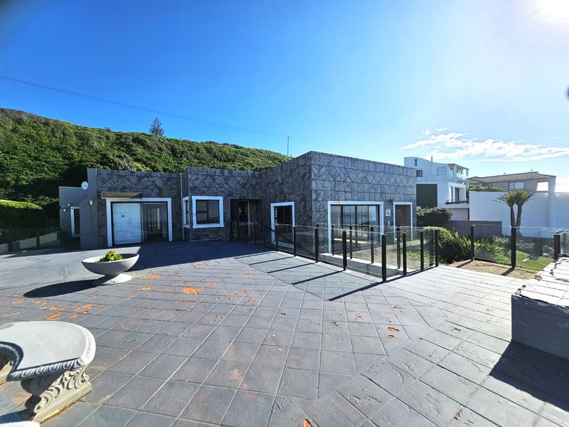 A spacious outdoor patio area featuring dark tiled flooring and glass balustrades, set against a modern exterior facade with stone-look cladding.