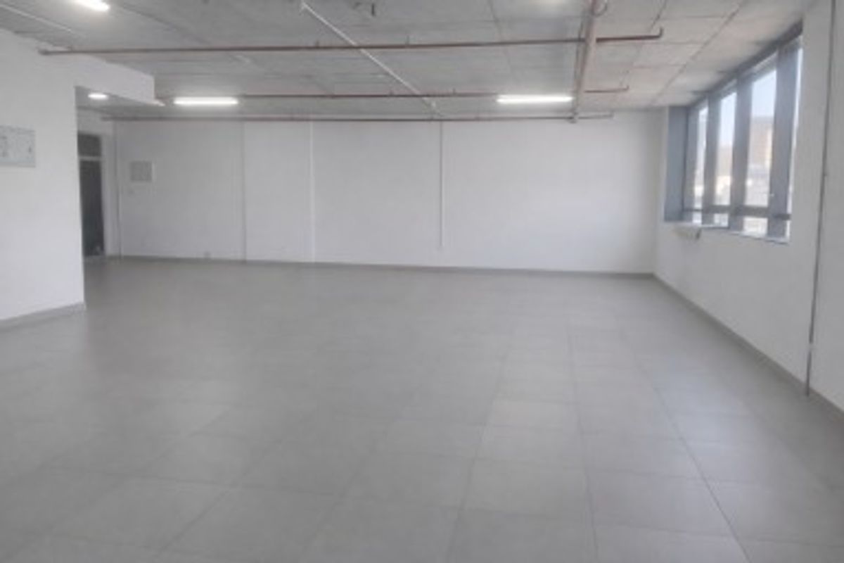 A spacious, vacant open-plan commercial office area featuring tiled flooring, large windows for natural light, and exposed ceiling infrastructure.