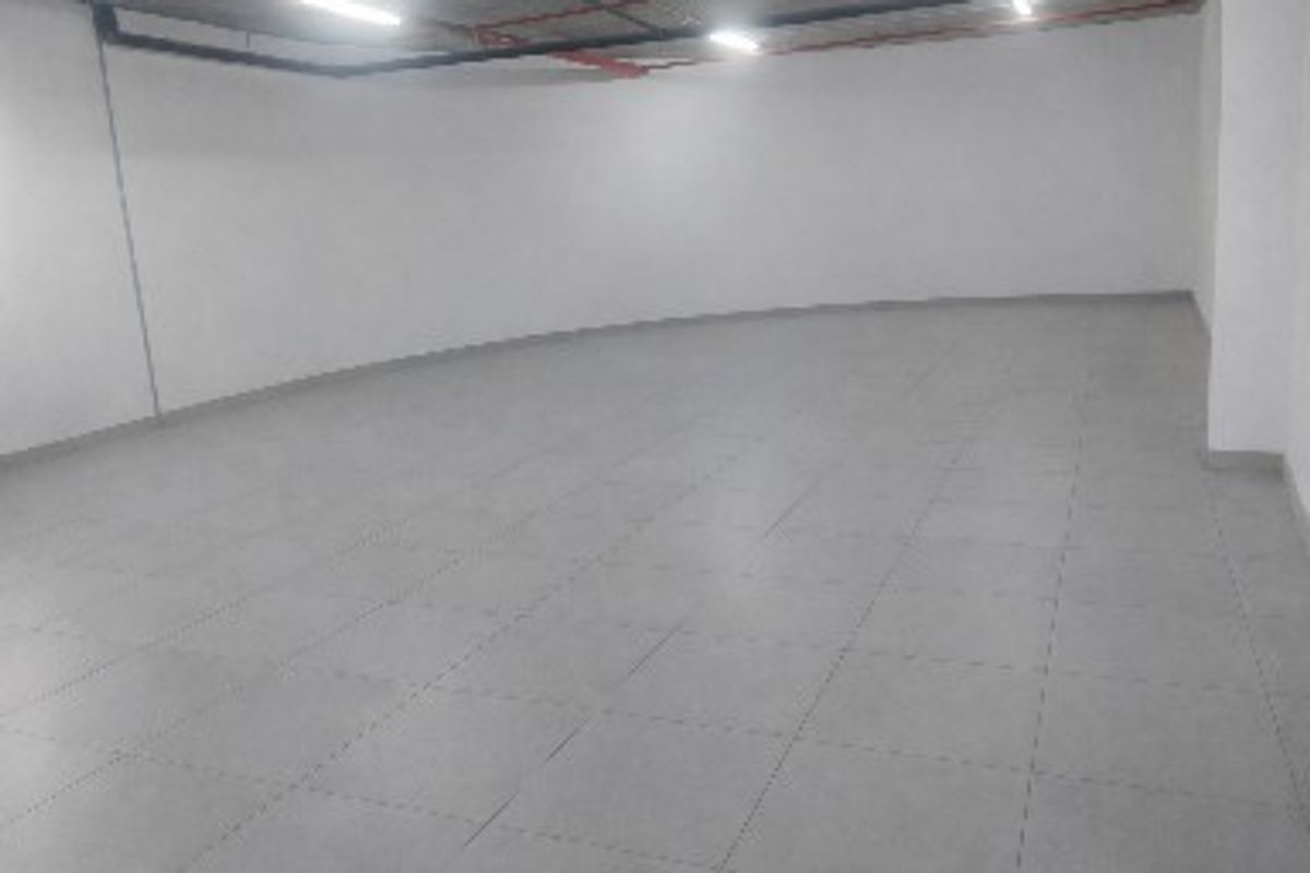 A spacious, empty commercial utility area featuring tiled flooring, exposed ceiling piping, and functional overhead lighting.