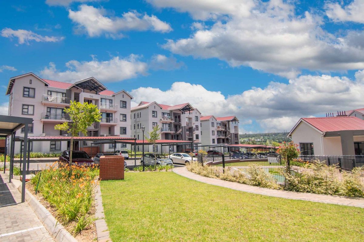 Exterior view of a modern apartment complex featuring multi-story buildings with metal roofs, covered parking carports, and well-maintained landscaped garden areas.