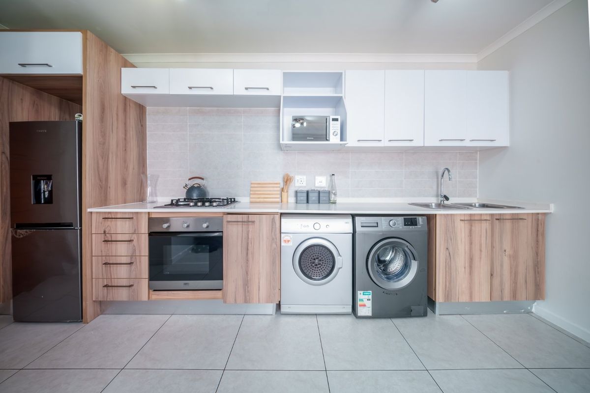 Modern kitchen featuring wood-grain and white cabinetry, stone countertops, built-in oven, gas hob, and integrated laundry appliance space with tiled flooring.