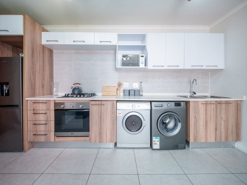 Modern kitchen featuring wood-grain and white cabinetry, stone countertops, built-in oven, gas hob, and integrated laundry appliance space with tiled flooring.