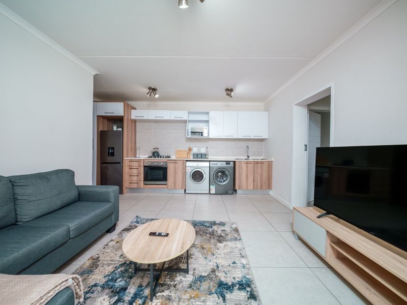 Modern open-plan living area featuring a contemporary kitchen with built-in cabinetry, integrated appliances, and neutral tiled flooring throughout.