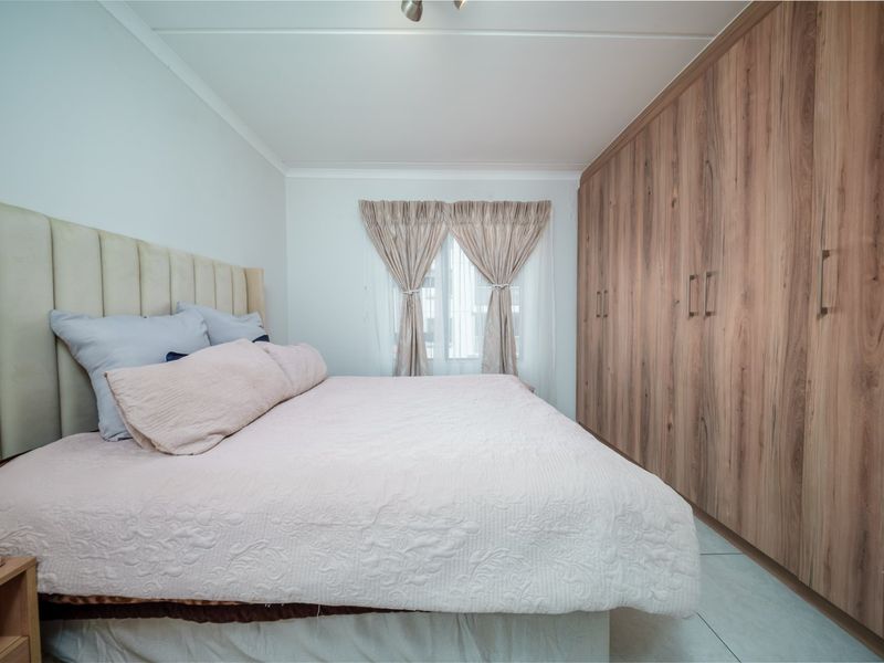 A well-maintained bedroom featuring extensive floor-to-ceiling built-in wooden cupboards, neutral tiled flooring, and a clean, modern aesthetic.