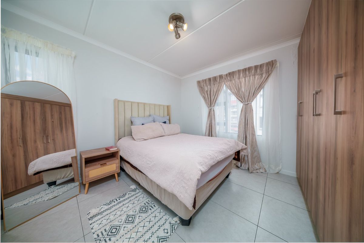 A well-maintained bedroom featuring neutral tiled flooring, built-in wooden cupboards, and ample natural light through the window.