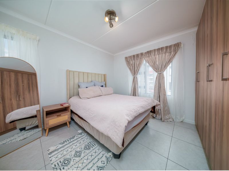 A well-maintained bedroom featuring neutral tiled flooring, built-in wooden cupboards, and ample natural light through the window.