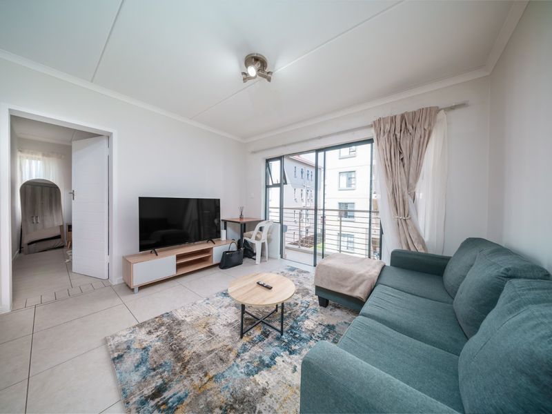 A bright living room featuring tiled flooring, neutral walls, and a sliding glass door providing access to a balcony.