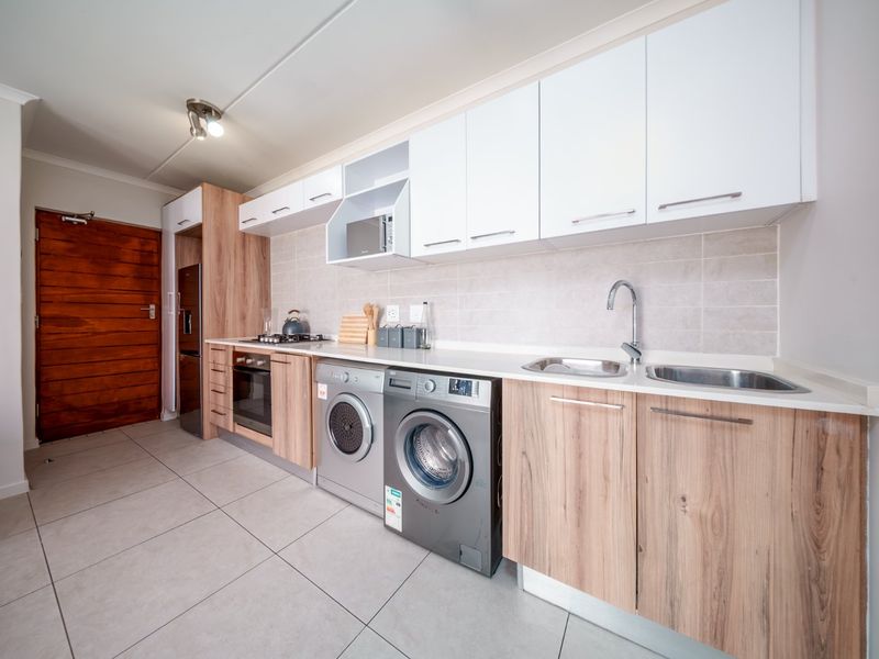 Modern kitchen featuring wood-grain and white cabinetry, stone countertops, integrated oven and hob, and tiled flooring with space for laundry appliances.