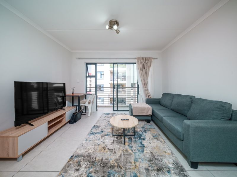 A bright and well-maintained living room featuring tiled flooring, a modern ceiling light, and a sliding glass door providing access to a private balcony.