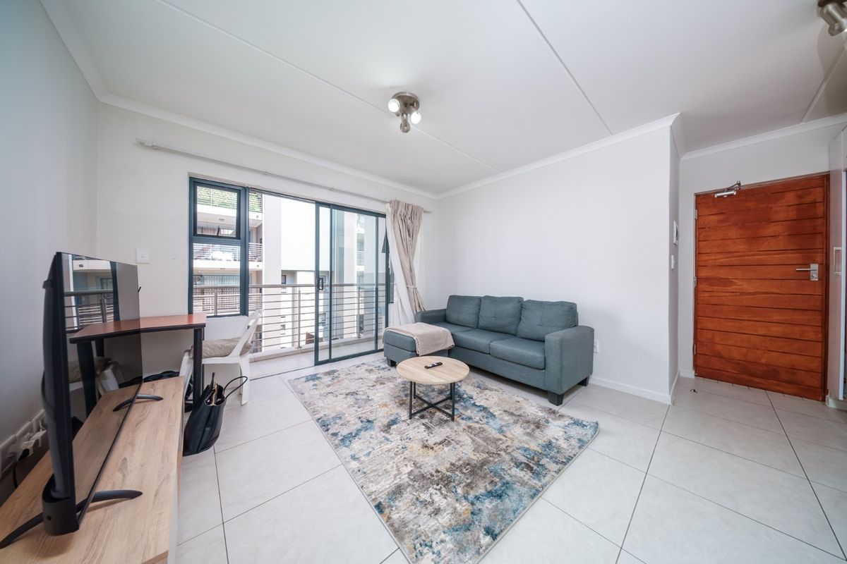A bright living room featuring large format floor tiles, a sliding glass door leading to a balcony, and a solid timber entrance door.