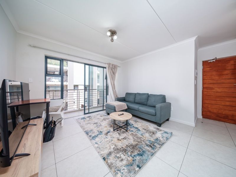 A bright living room featuring large format floor tiles, a sliding glass door leading to a balcony, and a solid timber entrance door.