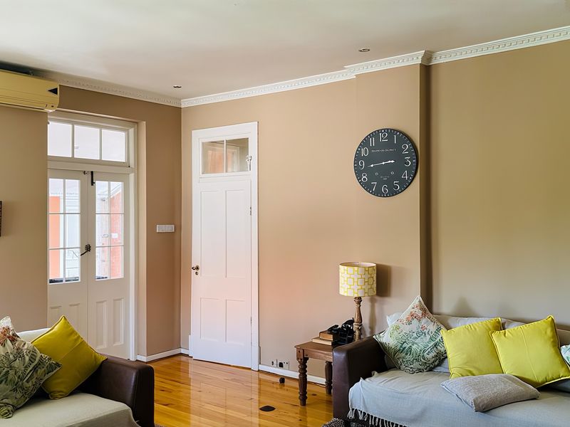 A well-maintained living room featuring polished hardwood floors, crown molding, and a wall-mounted air conditioning unit, providing a comfortable and inviting atmosphere.
