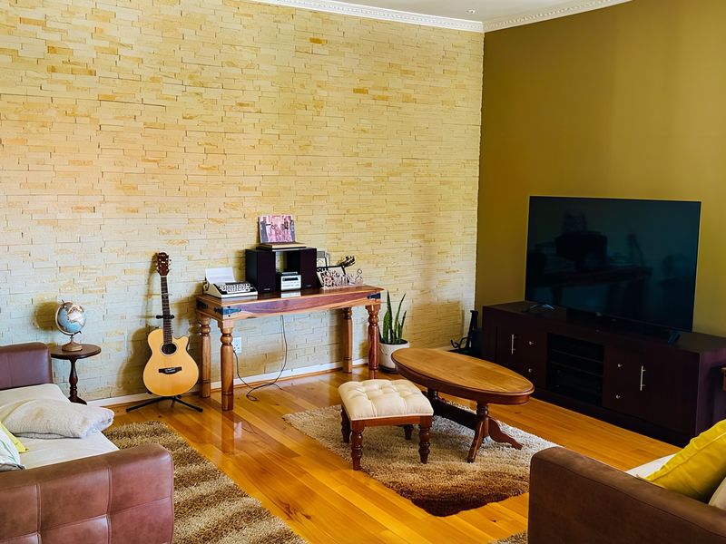 A comfortable living room featuring a textured stacked stone accent wall, warm hardwood flooring, and elegant crown molding.