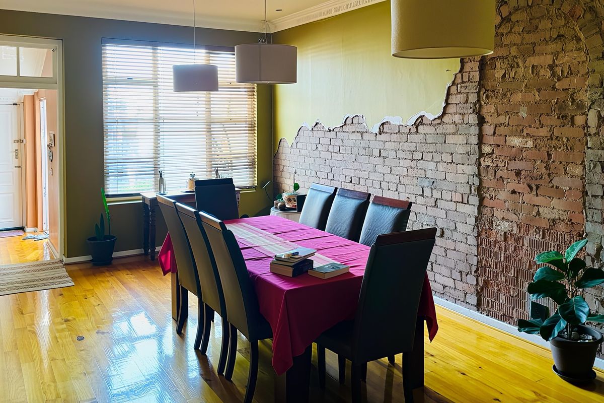 Dining room featuring polished hardwood floors, an exposed brick feature wall with partial plaster finish, and natural light through venetian blinds.
