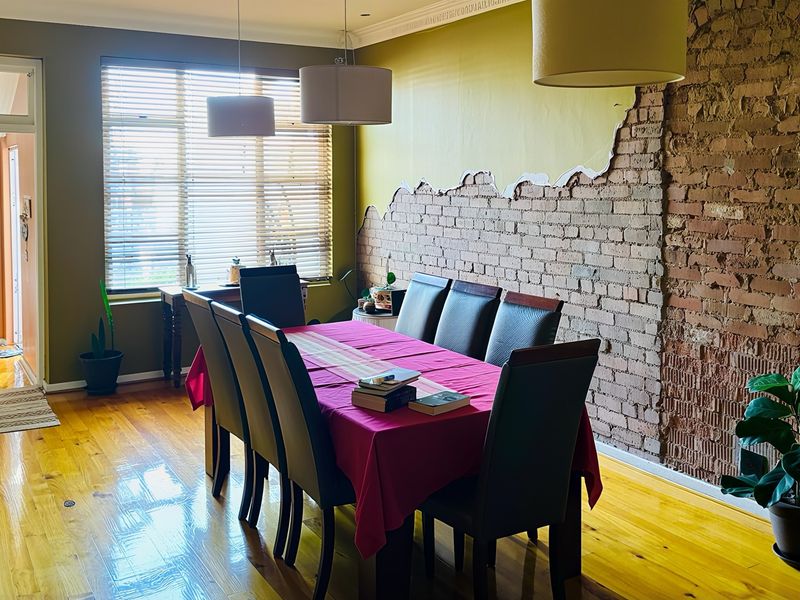 Dining room featuring polished hardwood floors, an exposed brick feature wall with partial plaster finish, and natural light through venetian blinds.