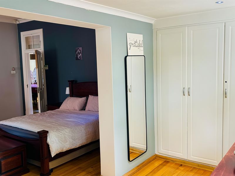 A bedroom featuring hardwood flooring, built-in wardrobes, and a connected living space, finished with coving and recessed lighting.
