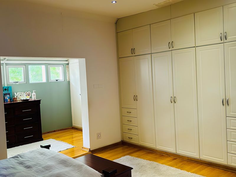 Spacious bedroom featuring extensive built-in cabinetry, warm hardwood flooring, and recessed lighting, with an adjoining alcove area.