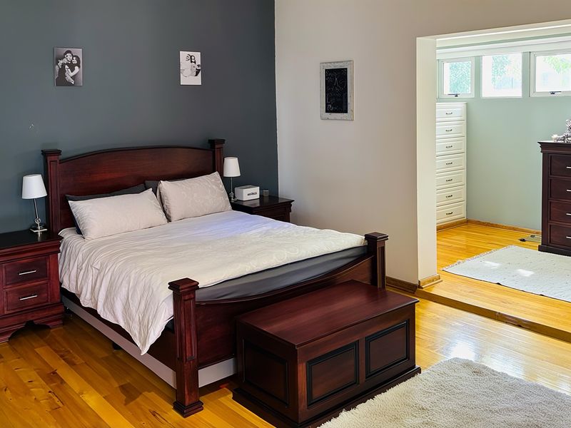 A spacious bedroom featuring polished hardwood flooring, a distinct raised floor area, and a neutral color palette with a dark accent wall.