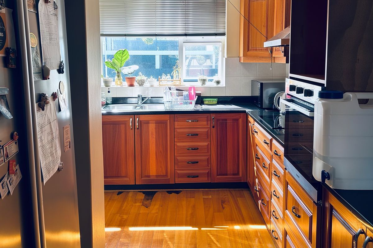 A functional kitchen featuring warm wooden cabinetry, granite countertops, built-in oven, and hardwood flooring, with a window providing natural light.