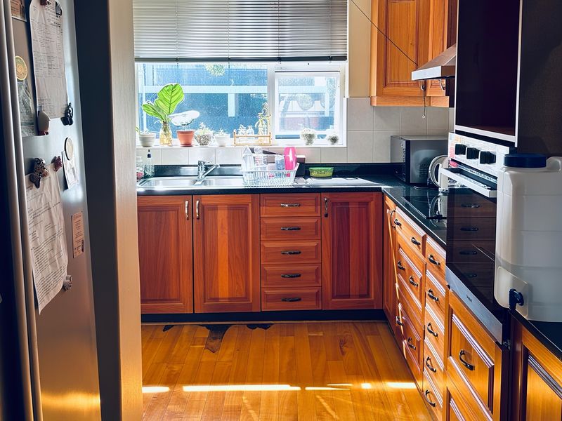 A functional kitchen featuring warm wooden cabinetry, granite countertops, built-in oven, and hardwood flooring, with a window providing natural light.