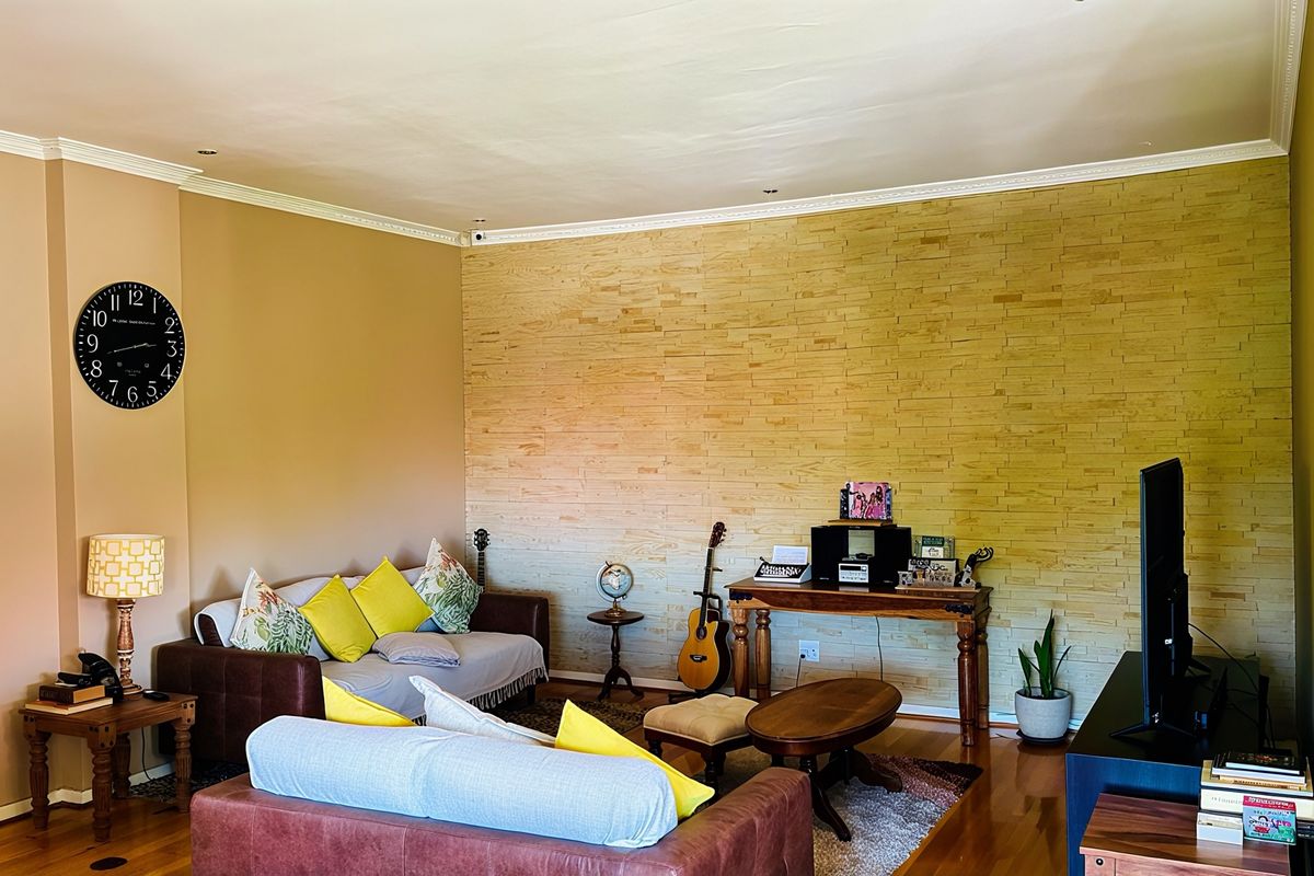 Spacious living room featuring a textured stone veneer accent wall, polished hardwood flooring, and decorative crown molding.