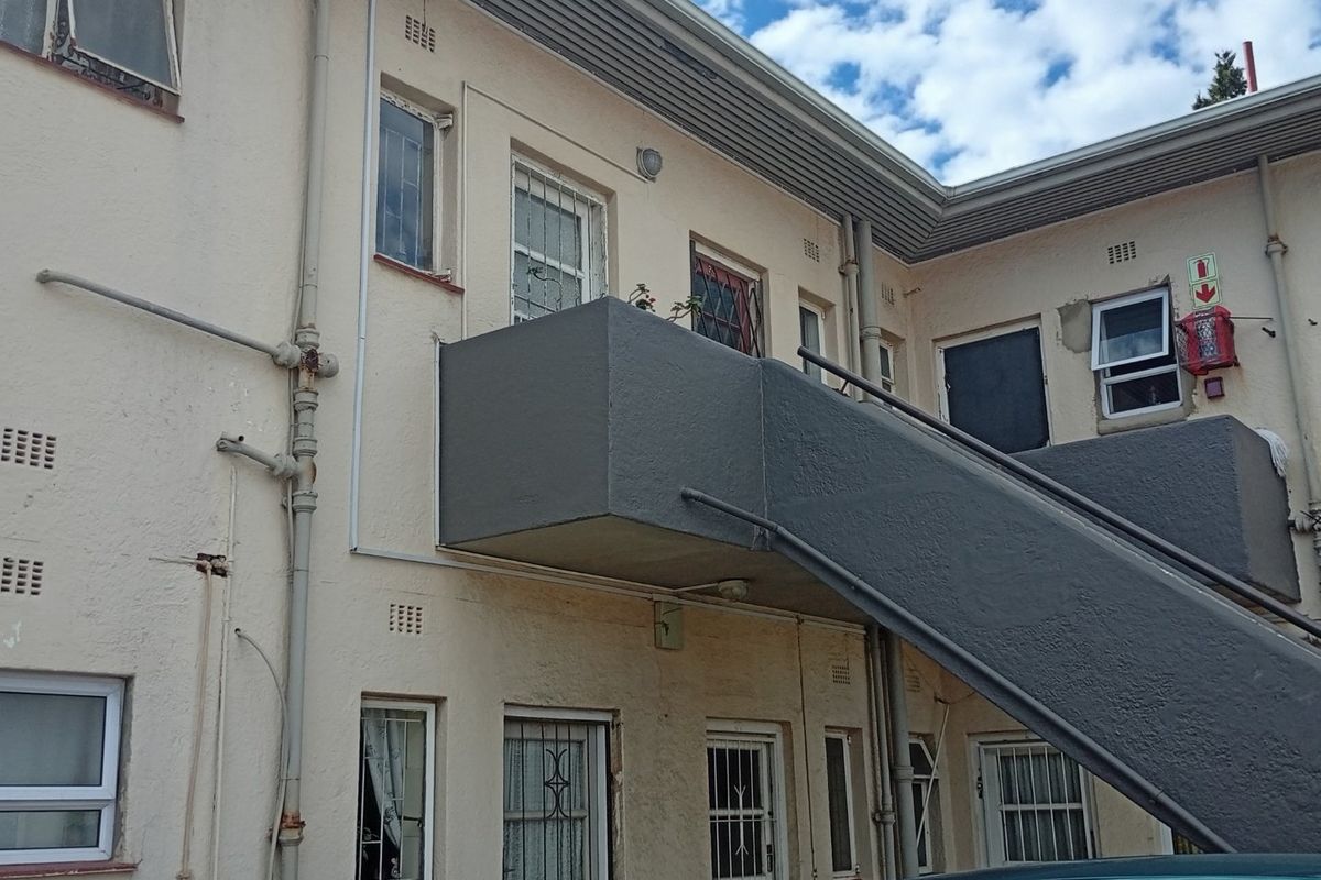 Exterior view of an apartment building featuring an external staircase, security bars on windows, and visible building maintenance requirements.