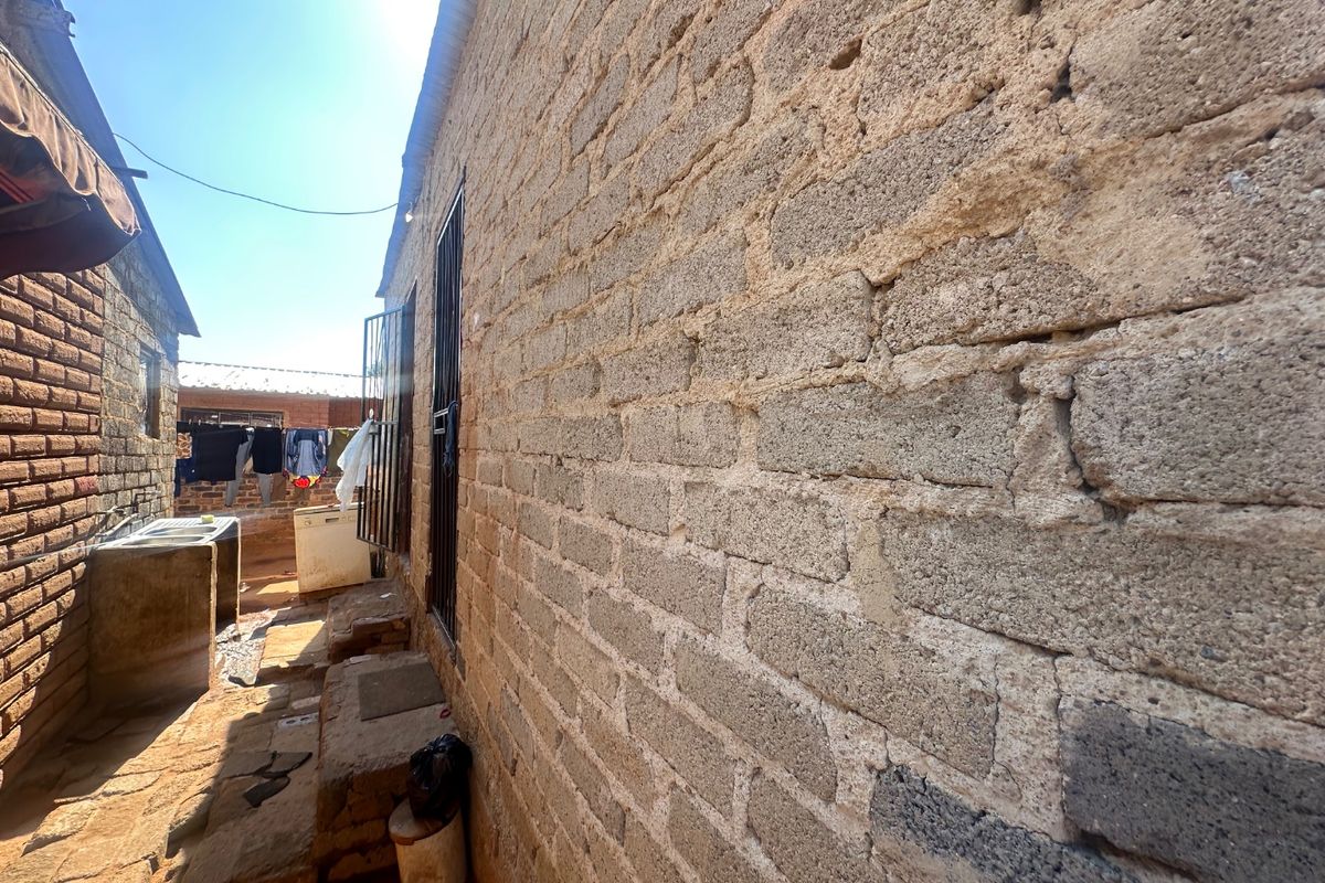 A narrow exterior side passage featuring exposed concrete block walls, security window bars, and a fixed concrete wash basin.