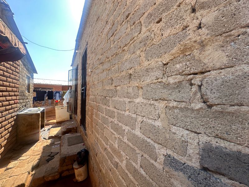 A narrow exterior side passage featuring exposed concrete block walls, security window bars, and a fixed concrete wash basin.