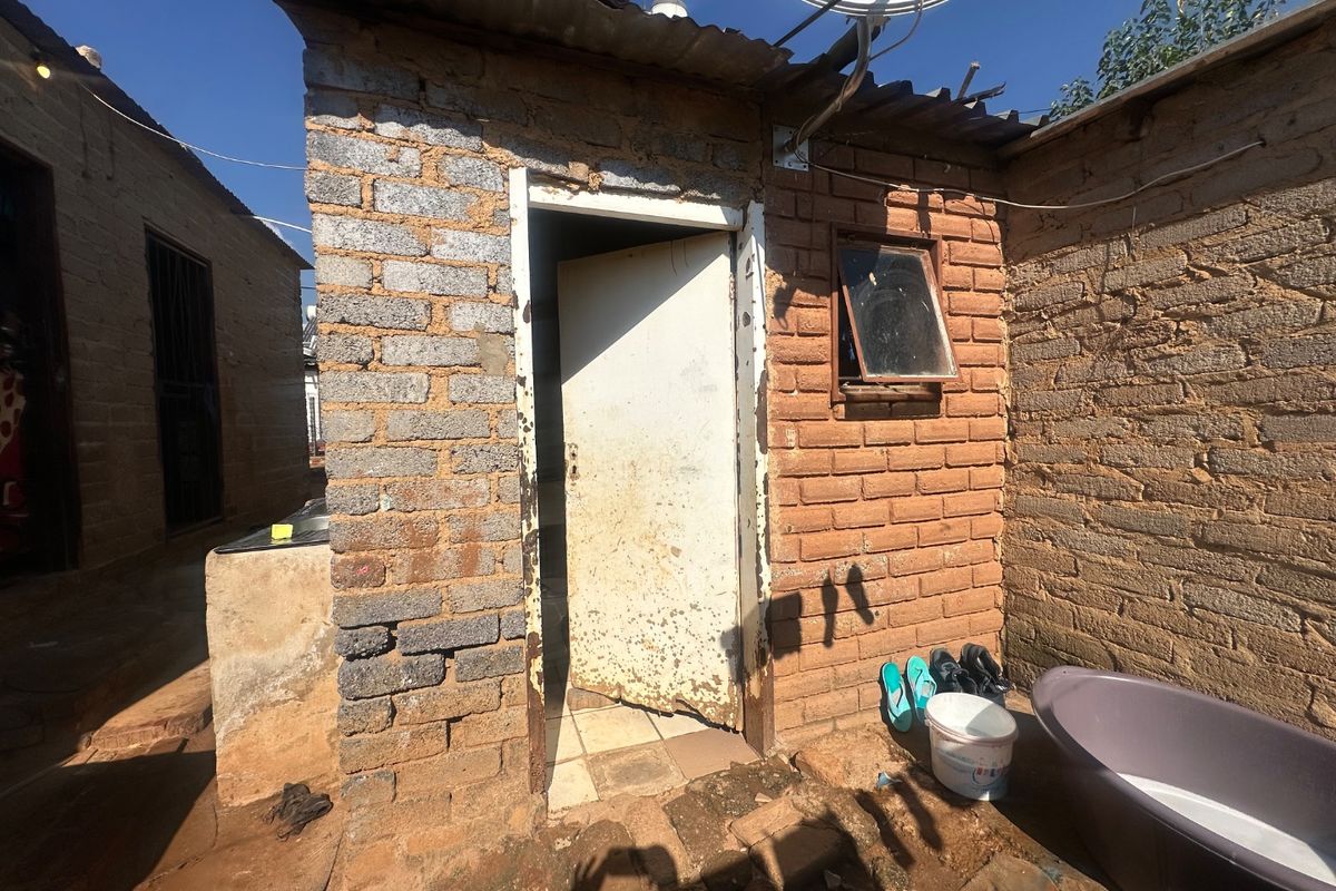 Exterior view of a small brick structure featuring a corrugated metal roof, satellite dish, and a weathered entrance door.