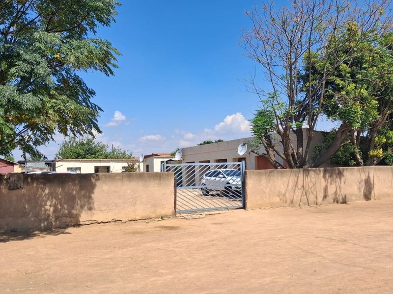 Front view of the property featuring a perimeter wall, metal entrance gate, and mature trees in the yard.