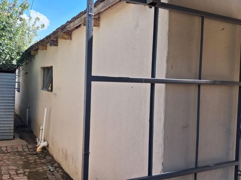 Rear exterior view of the property showing a side walkway, corrugated iron roofing, and a metal gate structure.
