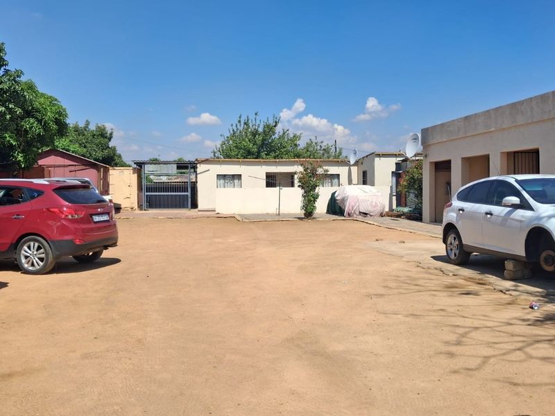 A spacious rear exterior area featuring a large unpaved driveway, concrete pathways, and multiple building access points with satellite dish installations.