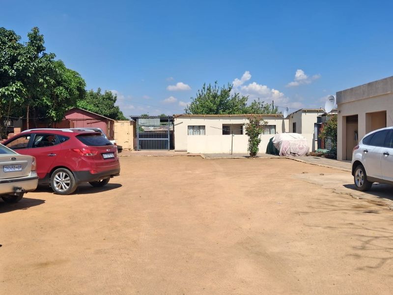 Front exterior view of the property featuring a large unpaved driveway area and multiple building structures.