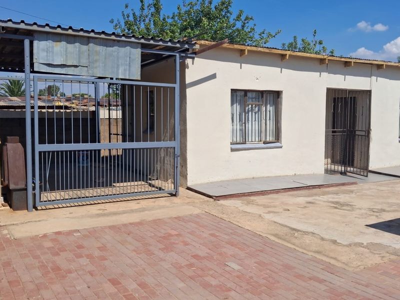 Front exterior view of the property featuring a paved driveway, metal security gate, and a simple structure with security bars on the windows.