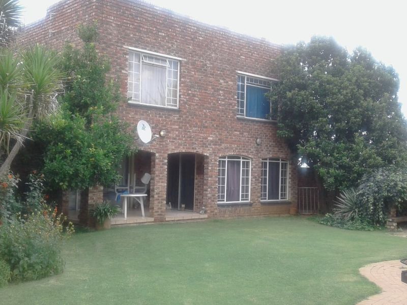 Rear view of a double-story face brick house featuring a covered patio, established garden, and a swimming pool with paved surround.