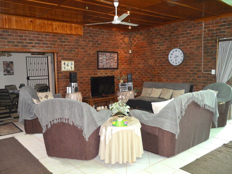 Spacious living room featuring exposed brick walls, a timber panelled ceiling with a ceiling fan, and tiled flooring with access to the exterior.