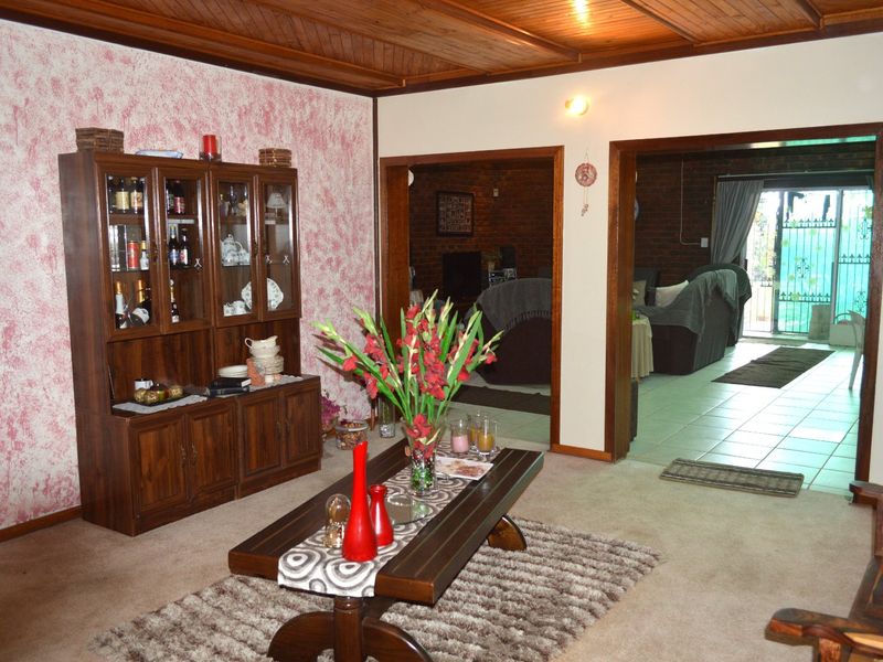 A living room featuring a timber ceiling and carpeted flooring, with open access to an adjacent living area with exposed brick walls and tiled floors.