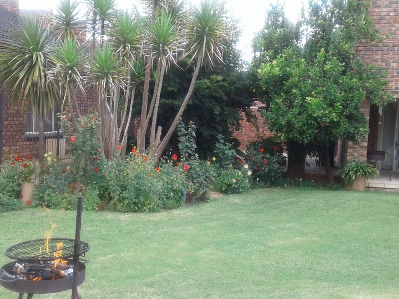 A private rear garden featuring a well-maintained lawn, mature landscaping, and a paved patio area adjacent to the brick-built house.