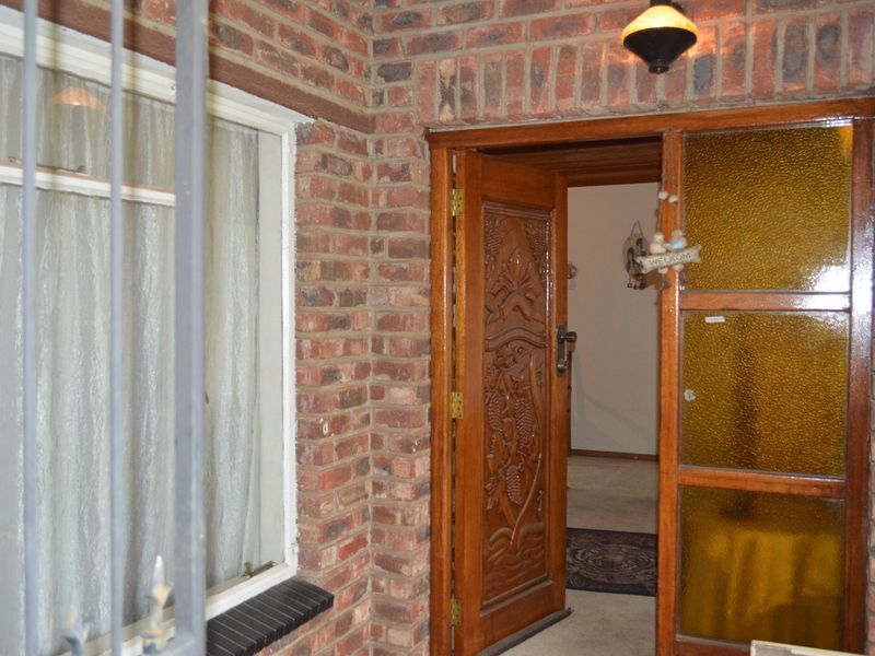 Entrance area featuring a decorative carved wooden door, textured glass sidelight, and exposed brick facade with security gate.