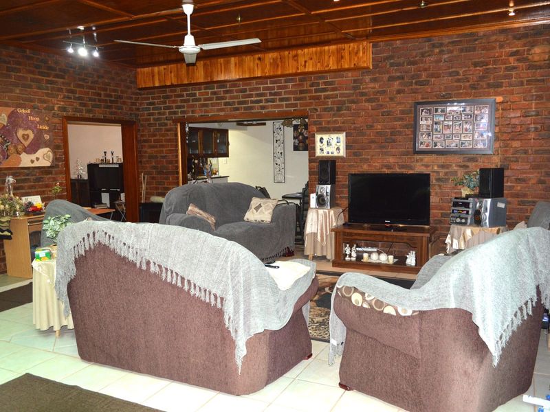 Spacious living room featuring rustic exposed brick walls, a warm timber panelled ceiling, and neutral tiled flooring, offering a cozy and traditional atmosphere.